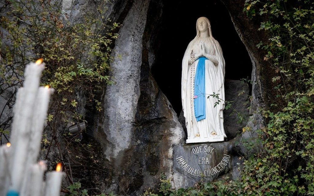 Estatua de la Virgen de Lourdes con manto blanco y manos unidas, dentro de la gruta